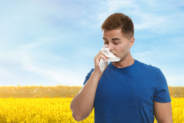 Young man suffering from allergy and blooming field on background