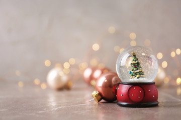 Snow globe with Christmas tree and decorations on marble table against festive lights, space for...