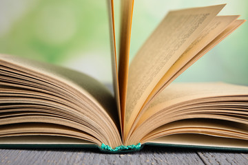 Open book on grey wooden table against blurred green background, closeup