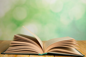 Open book on wooden table against blurred green background. Space for text