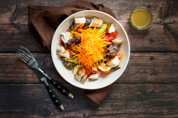 Salad with grilled chicken breast, carrot, red onion and roasted vegetables with dressing on dark rustic wooden table