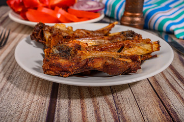 Lamb ribs marinated with spices grilled in a plate on the table. With sliced tomatoes, sweet peppers and onions.