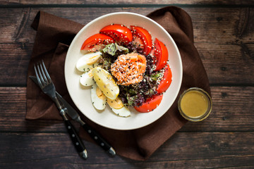 Salad with smoked salmon, sesame seeds, tomatoes and egg with dressing on rustic wooden table