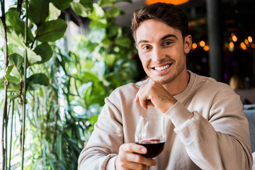 happy man holding glass with red wine while looking at camera