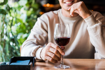 cropped view of cheerful man sitting in restaurant with glass of wine