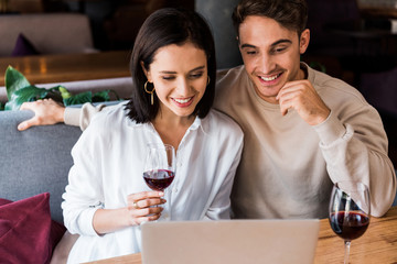 happy man and woman with glass of wine looking at laptop