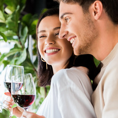 happy man holding glass with red wine near beautiful girl