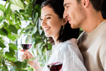 selective focus of handsome man holding glass with red wine near positive girl