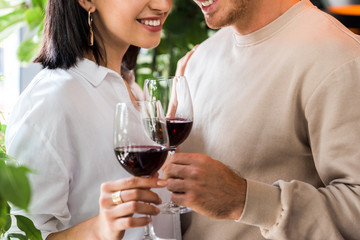 cropped view of happy man holding glass with red wine near cheerful girl