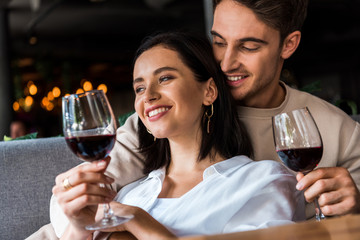 happy man holding glass with wine near cheerful woman