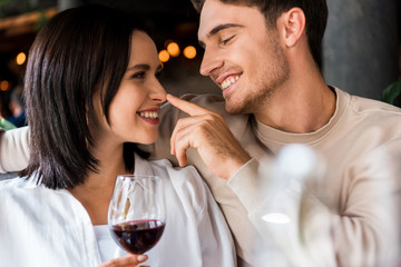 happy man touching nose of girlfriend with red wine in glass