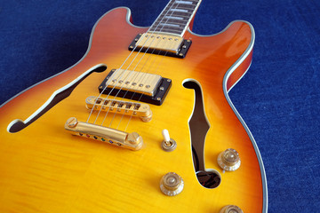 Vintage semi-hollow body jazz electric guitar with golden pickups, electronics knobs and metal accessories on blue jeans background close up