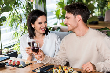 happy man and woman clinking glasses with red wine near sushi
