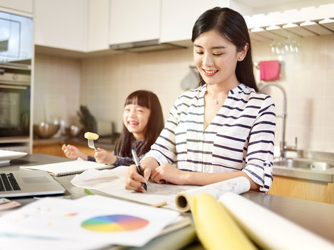 asian woman working at home while taking care of daughter