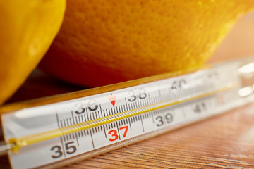 Thermometer close up on a background of yellow lemons lying on a brown table