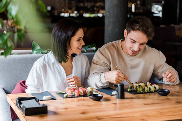 selective focus of happy man and woman near tasty sushi in restaurant