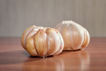 Two unpeeled ripe heads of garlic close up lie on a wooden table