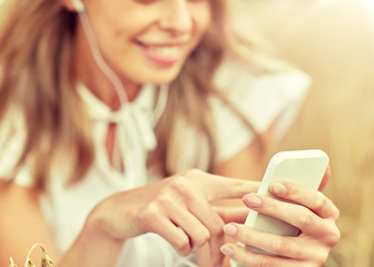 summer holidays, vacation, technology and people concept - close up of smiling young woman in white dress with smartphone and earphones listening to music on cereal field