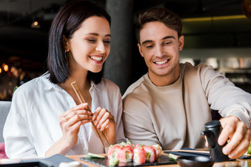 cheerful man holding black bottle near woman and sushi