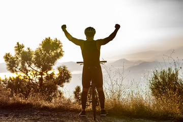 silhouette of male biker raising hands for victory