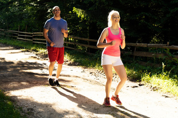 Running fitness couple of runners doing sport on road outdoor. Active living man and woman jogging training cardio in summer outdoors nature.