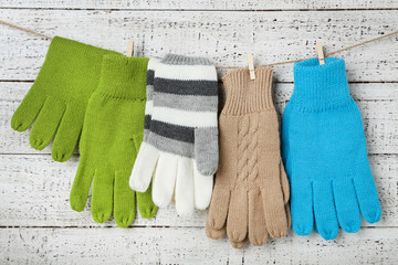 Knitted mittens hanging on white wooden background
