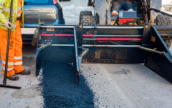 Worker regulate laying new asphalt to patch a bump in the road.