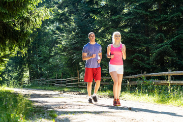 Fototapeta na wymiar Running fitness couple of runners doing sport on road outdoor. Active living man and woman jogging training cardio in summer outdoors nature.