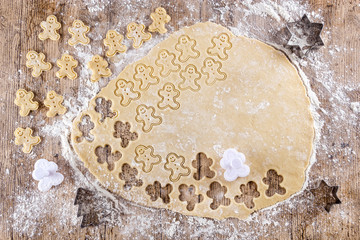 Top view of raw dough that is being cut to make cookies shaped like funny gingerbread dolls on a floured wooden table. View from above. Funny food concept. Recipes for children. Christmas desserts.
