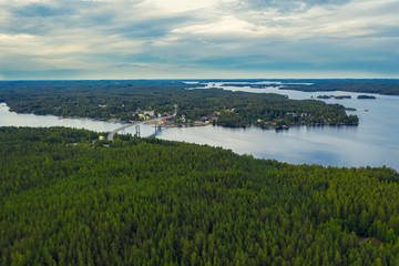 Aerial view on the bridge over the lake and trees in the forest on the shore. Blue lakes, islands and green forests from above on a cloudy summer day. Lake landscape in Finland, Puumala.