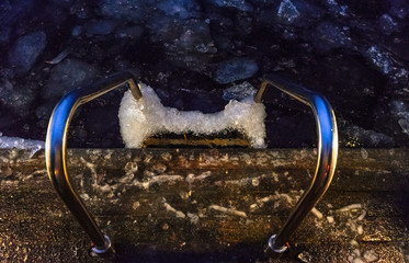 metal stairs to the dark water with floating ice of the winter lake at night