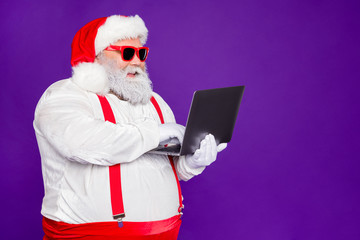 Profile side view portrait of his he nice confident cheerful cheery bearded Santa holding in hands laptop typing browsing wi-fi isolated over bright vivid shine vibrant violet lilac background