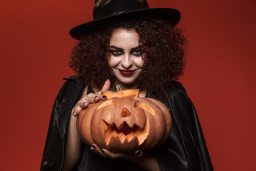 Image of curly witch girl in halloween costume holding carved pumpkin