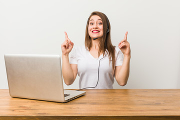 Young telemarketer woman indicates with both fore fingers up showing a blank space.