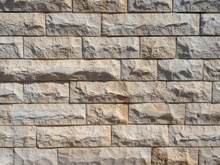 A fragment of a wall lined with roughly machined stone. Gray and pink cladding in midday sunlight.