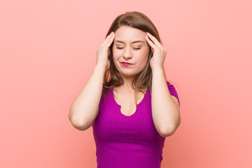 Young hispanic woman against a pink wall touching temples and having headache.