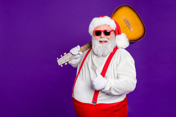 Fototapeta na wymiar Portrait of his he nice funny cool cheery glad cheerful bearded thick fat Santa carrying guitar showing thumbup isolated over bright vivid shine vibrant violet lilac background