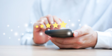 close up on customer man hand pressing on smartphone screen with gold five star rating feedback...