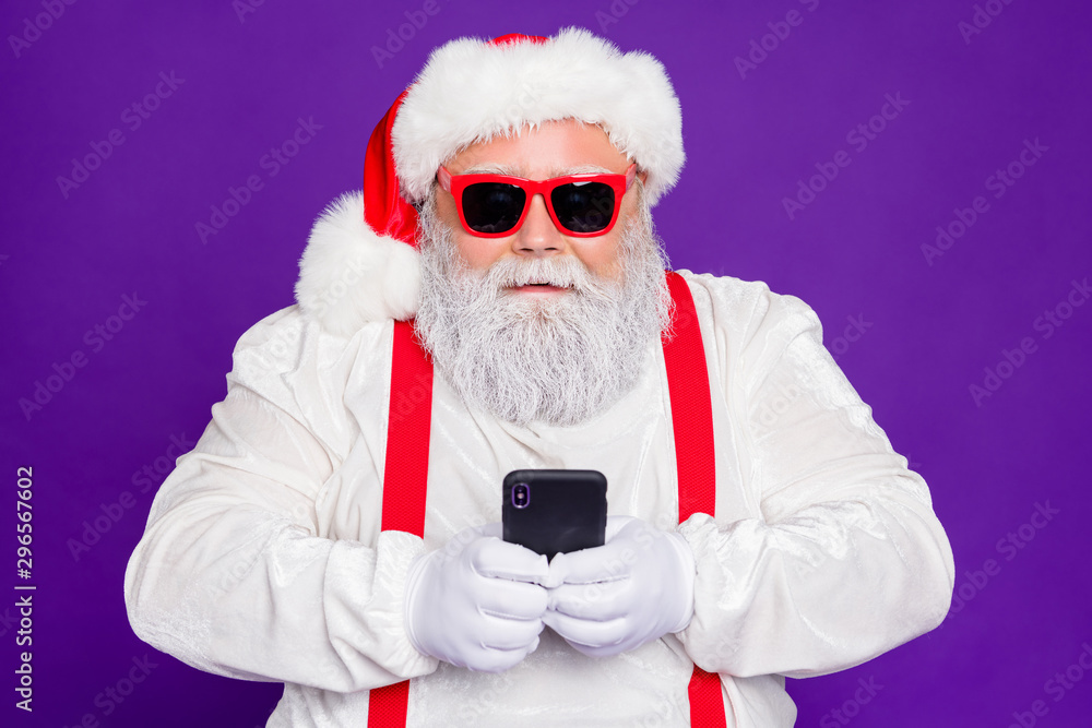 Sticker Photo of grey haired santa father holding telephone modern technology user checking newyear presents orders wear sun specs costume isolated purple background