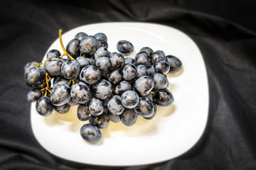 Fresh grapes on a branch lying on a white plate