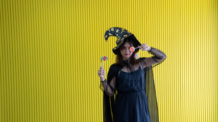 happy vivid young women catch candy booth 2 hands in black witch , women cute be delightful.Halloween costume on party over yellow background