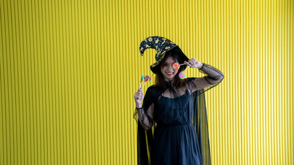 happy vivid young women catch candy booth 2 hands in black witch , women cute be joyful .Halloween costume on party over yellow background