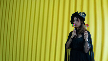 happy vivid young women catch candy booth 2 hands in black witch , women cute be cheerful.Halloween costume on party over yellow background