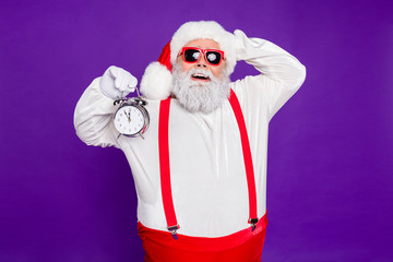 Photo of funny overweight santa father holding alarm clock remind it's newyear o'clock overjoyed wear sun specs hat suspenders isolated purple background