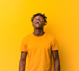 Young black man wearing rastas over yellow background relaxed and happy laughing, neck stretched...