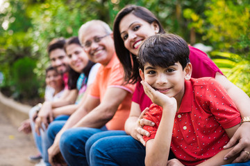 Indian Family enjoying Picnic - Multi generation of asian family sitting over or near small wall in park, outdoor. selective focus