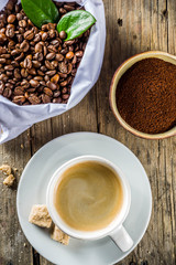 Cup of espresso with coffee beans. ground coffee and leaves on rustic background