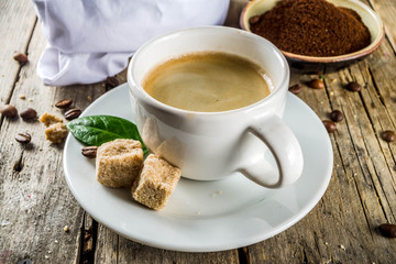 Cup of espresso with coffee beans. ground coffee and leaves on rustic background