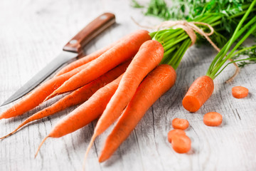 Fresh carrots bounded in bunch with one cut on white board and old knife in background.