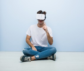 Teenager caucasian man using a virtual reality glasses sitting on the floor